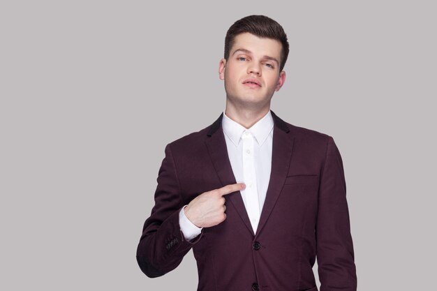 C'est moi. Portrait de fier beau jeune homme d'affaires en costume violet et chemise blanche, debout, regardant la caméra et se pointant et se vantant. tourné en studio intérieur, isolé sur fond gris