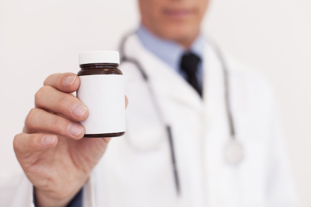 C'est ce qu'il vous faut ! Image recadrée d'un médecin en uniforme blanc étirant un flacon de médicament et debout isolé sur blanc