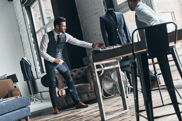 C'est de quoi j'ai besoin. Deux jeunes hommes à la mode ayant une discussion en se tenant debout en atelier