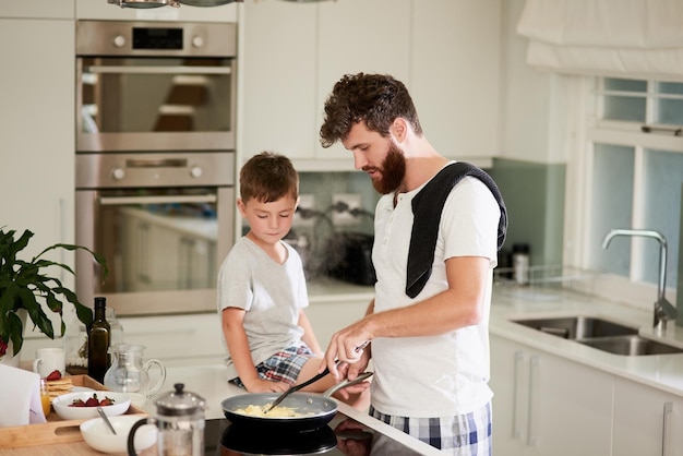 Et c'est le secret des œufs brouillés moelleux Photo d'un adorable petit garçon et de son père qui préparent le petit-déjeuner ensemble à la maison