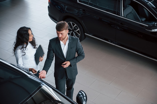 C'est un véhicule tout neuf. Cliente féminine et homme d'affaires barbu élégant et moderne dans le salon automobile.