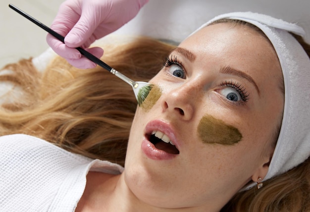 Esthéticienne appliquant un masque d'argile sur le visage d'une belle femme Traitement spa et soins du visage dans le salon de beauté