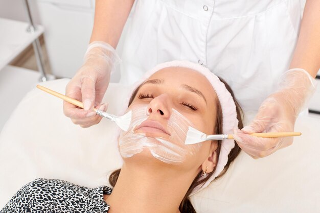 Esthéticienne appliquant un masque de crème cosmétique sur le visage de la femme pour une procédure de rajeunissement dans un salon de beauté