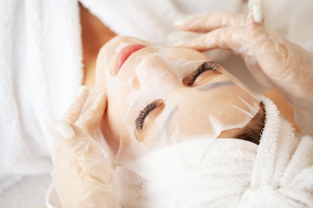 Esthéticienne appliquant un masque en feuille sur une femme dans un salon de spa