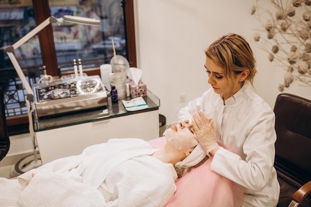 Esthéticienne appliquant un masque en feuille sur le visage d'une femme dans un salon de beauté