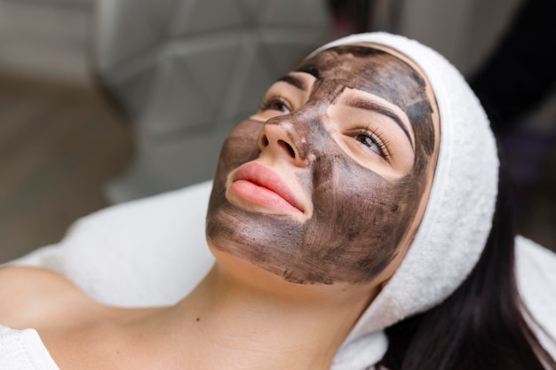 Esthéticienne appliquant un masque noir sur un joli visage de femme portant des gants noirs magnifique femme dans un spa ayant des procédures faciales