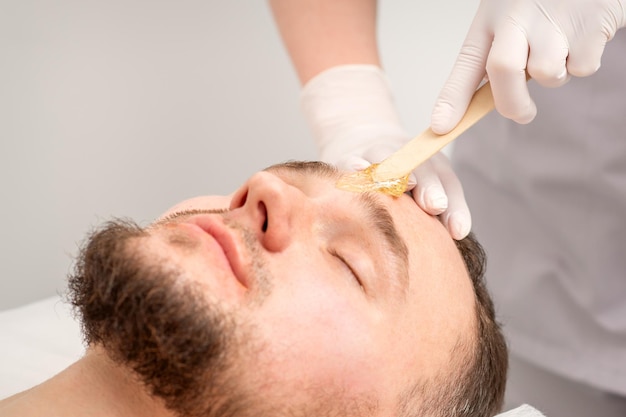 Esthéticienne appliquant la pâte de cire entre les sourcils pendant la procédure d'épilation à la cire dans le salon de beauté.