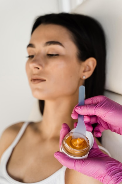 L'esthéticienne applique un masque facial lifting doré pour stimuler les processus naturels de renouvellement de la peau et restaurer l'élasticité du visage