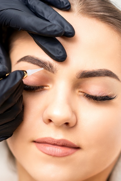 Esthéticienne, appliquer le maquillage permanent sur les sourcils de la jeune femme