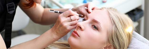 Esthéticienne construire un client de fille en forme de sourcil naturel. Le tatouage des sourcils est effectué à l'aide d'une machine à maquillage permanente. Effet après microblading. Maquillage indélébile. Voyage au salon de beauté pour correction