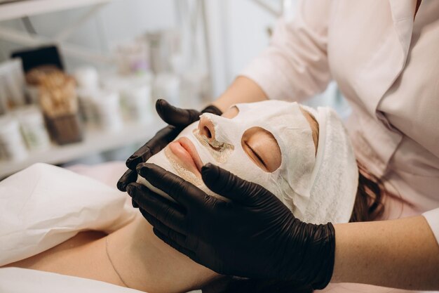 Esthéticienne couvrant la peau du visage de la femme avec un masque hydratant pendant la procédure de soin de la peau