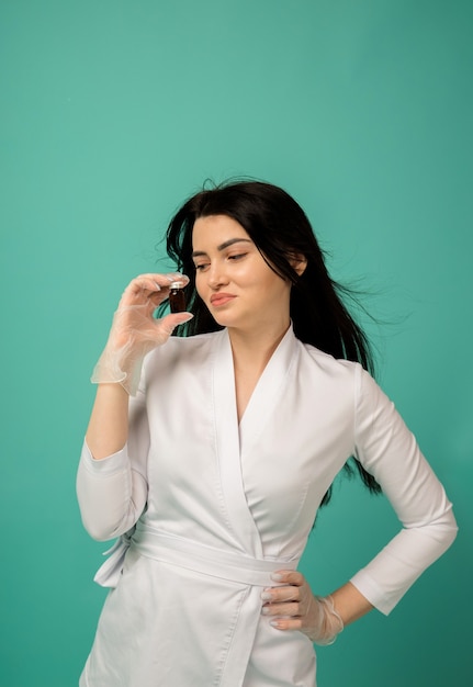 Une esthéticienne dans un costume blanc et des gants transparents détient un médicament sur turquoise