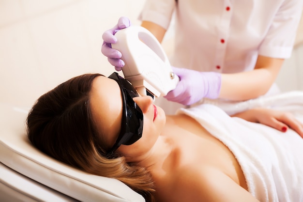 Esthéticienne donnant un traitement d'épilation au laser au visage d'une jeune femme à la clinique de beauté.