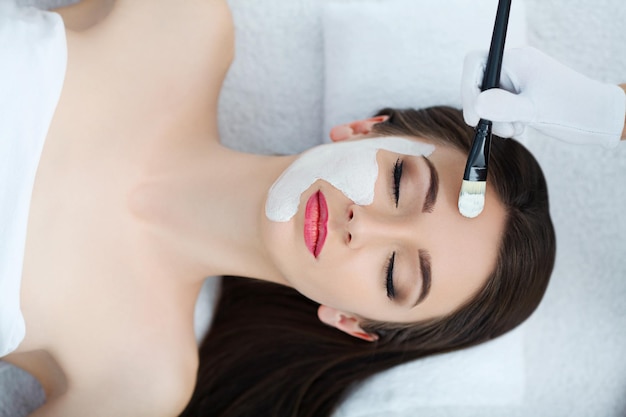 L'esthéticienne du spa applique le masque sur le visage d'une belle jeune femme dans les soins spa du salon spa