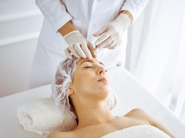 Esthéticienne effectuant une procédure de beauté avec une seringue sur le visage d'une jeune brune. Médecine cosmétique et chirurgie, injections de beauté.