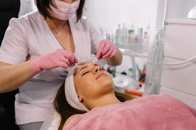 L'esthéticienne enlève un masque d'argile du visage d'une jeune fille dans le salon Spa Belle jeune fille à l'esthéticienne fait les procédures du spa