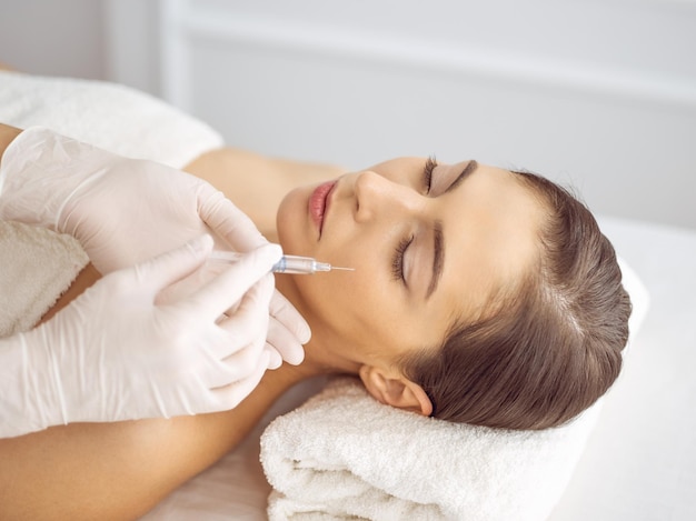 Photo esthéticienne faisant une procédure de beauté avec une seringue sur le visage d'une jeune femme brune. médecine et chirurgie esthétiques, injections de beauté.