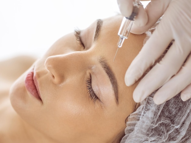 Photo esthéticienne faisant une procédure de beauté avec une seringue sur le visage d'une jeune femme brune. médecine et chirurgie esthétiques, injections de beauté.