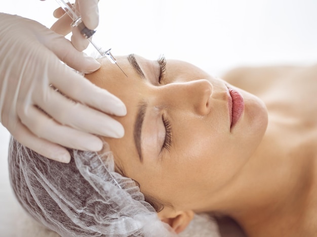Esthéticienne faisant une procédure de beauté avec une seringue sur le visage d'une jeune femme brune. Médecine et chirurgie esthétiques, injections de beauté.