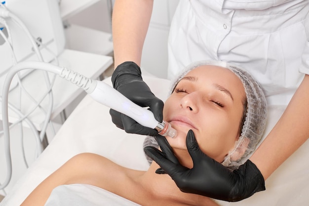 L'esthéticienne fait une exfoliation à l'eau pour la procédure de soins de la peau du visage de la femme de rajeunissement dans un salon de beauté