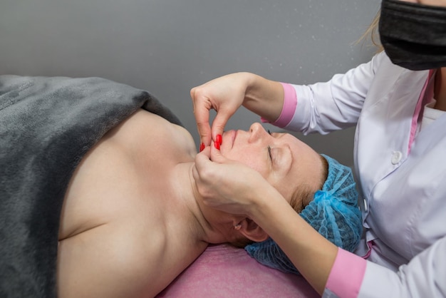 Une esthéticienne fait un massage du visage à une femme dans un salon de beauté. Le concept de soins du visage, procédures cosmétiques.