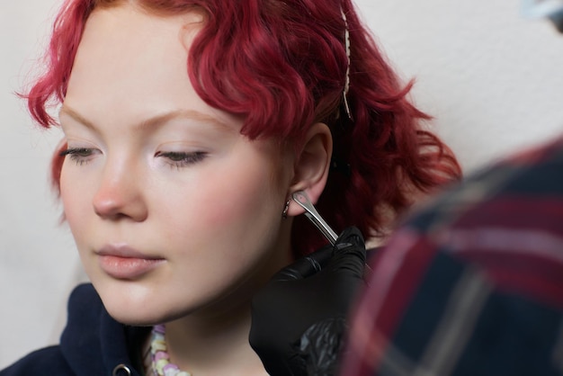 Une esthéticienne fait une ponction du lobe de l'oreille avec un appareil jetable dans un salon de beauté. Lobe de perçage des oreilles.