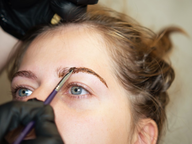 Photo l'esthéticienne maquilleuse applique de la peinture au henné sur les sourcils. soins du visage professionnels.