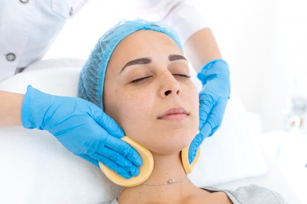 L'esthéticienne nettoie le visage du patient avec des éponges avant d'appliquer le masque pour les soins de la peau