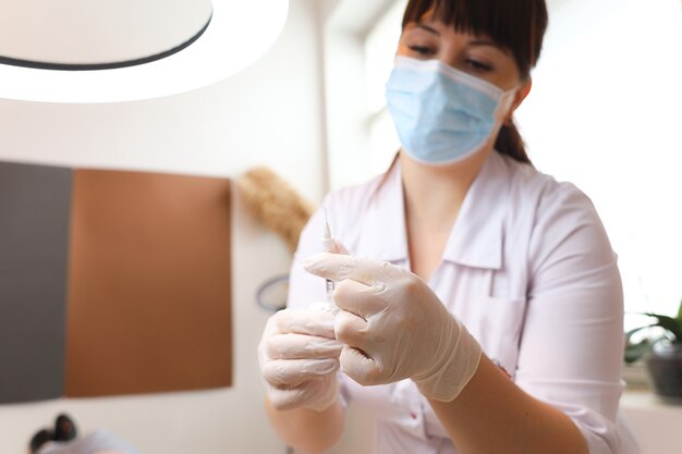 Une esthéticienne portant des gants blancs stériles tient une charge d'injection d'acide hyaluronique et la regarde