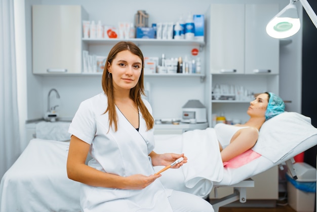 Photo esthéticienne près d'une patiente sur une table de traitement, préparation d'injection de botox. procédure de rajeunissement dans un salon d'esthéticienne. médecin et femme, chirurgie esthétique contre les rides et le vieillissement