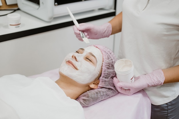 Une esthéticienne professionnelle applique un masque facial sur le visage des clients dans un centre de beauté spa jeune femme