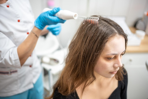 Esthéticienne professionnelle faisant la procédure de traitement des cheveux darsonval pour jeune femme dans un salon de beauté