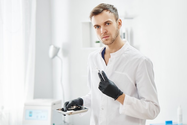 Une esthéticienne professionnelle masculine adulte avec une seringue à la main se prépare à l'injection dans le contexte du salon de beauté