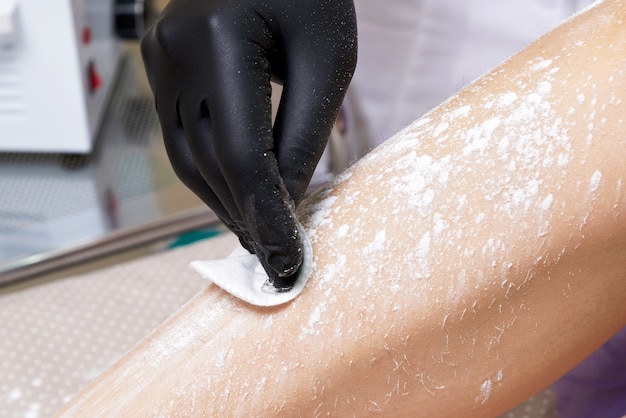 Esthéticienne se prépare à épiler les jambes féminines dans le centre de spa. Préparation à l'épilation, mettre de la poudre blanche