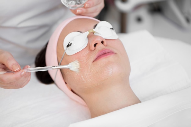 Esthéticienne en soins de la peau du visage appliquant un masque à l'huile de beauté sur le visage à l'aide d'une brosse dans un salon de spa