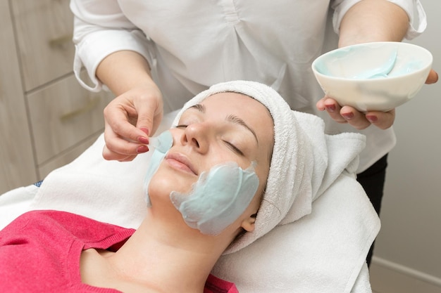 Esthéticienne en soins de la peau du visage appliquant un masque à l'huile de beauté sur le visage à l'aide d'une brosse dans un salon de spa