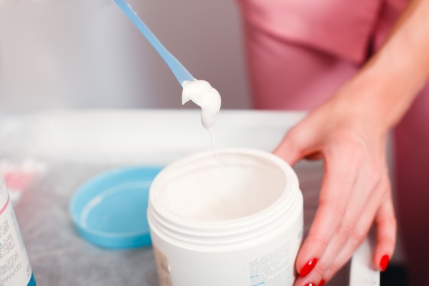 L'esthéticienne tient en mains un pot de crème cosmétique et une spatule. Soins de la peau et du corps.