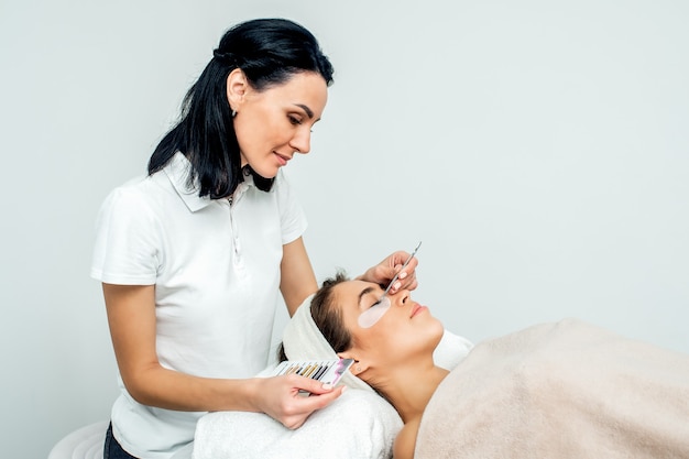 Esthéticienne travaillant pendant la procédure d'extension de cils avec patient sur fond blanc avec copie