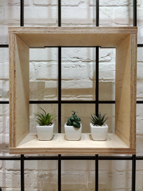 Une étagère carrée en bois décorative avec trois pots pour différents pots de fleurs est accrochée au mur de briques