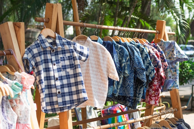 Photo des étagères de vêtements en bois avec des chemises à manches courtes colorées sur des cintreaux des vêtements sur le marché de rue