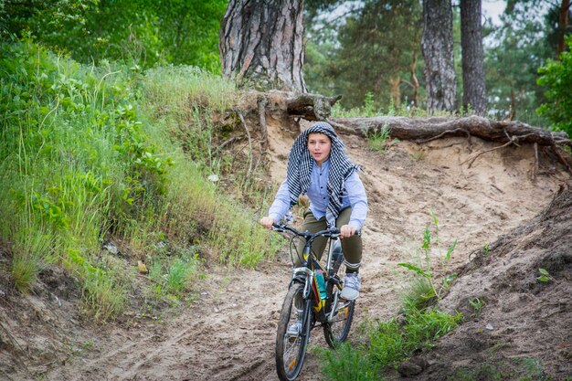 Photo en été, dans une forêt de pins, un garçon fait du vélo en bas de la montagne