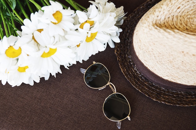 L'été est là! Chapeau de paille élégant, lunettes de soleil et fleurs de camomille.