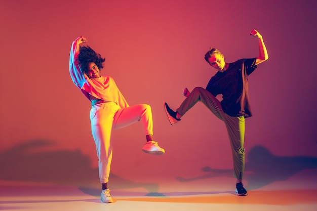 L'été. Homme Et Femme élégants Dansant Le Hip-hop Dans Des Vêtements Lumineux Sur Fond Vert à La Salle De Danse à La Lumière Du Néon. Culture Jeunesse, Mouvement, Style Et Mode, Action. Portrait à La Mode.