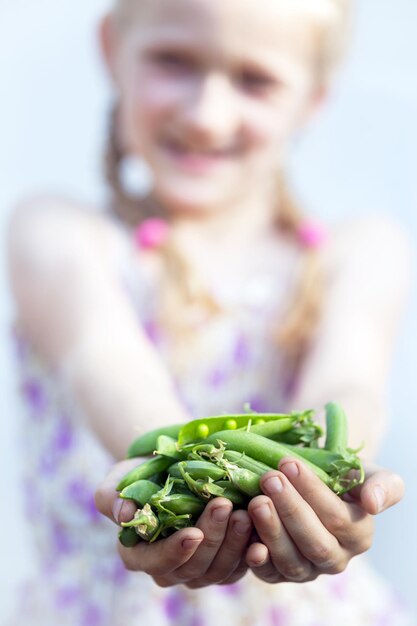 Été - la jeune fille souriante tient un pois vert dans ses mains