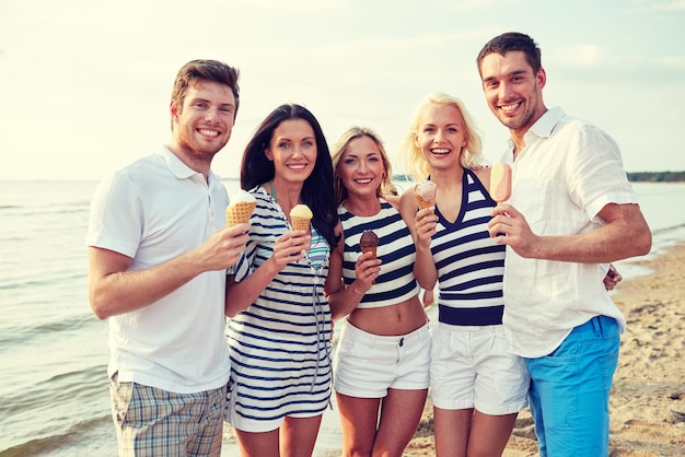 été, vacances, mer, tourisme et concept de personnes - groupe d'amis souriants mangeant des glaces sur la plage