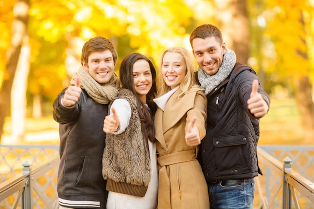 été, vacances, vacances, concept de personnes heureuses - groupe d'amis ou de couples s'amusant et montrant les pouces vers le haut dans le parc d'automne