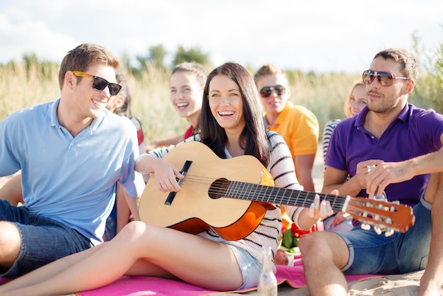 été, vacances, vacances, musique, concept de gens heureux - groupe d'amis avec guitare s'amusant sur la plage