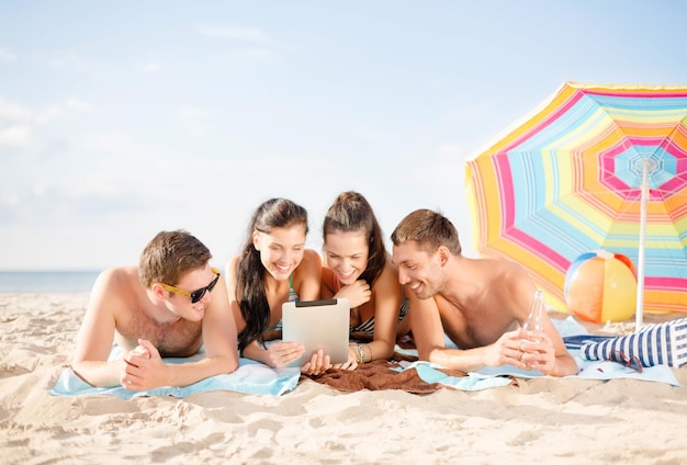 été, vacances, vacances, technologie et concept de personnes heureuses - groupe de personnes souriantes avec tablette sous un parapluie sur la plage