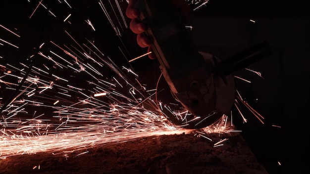 Des étincelles lumineuses d'une circulaire dans l'obscurité sur un fond noir libre Un travailleur coupe le métal avec une scie circulaire libre Travailler avec du fer