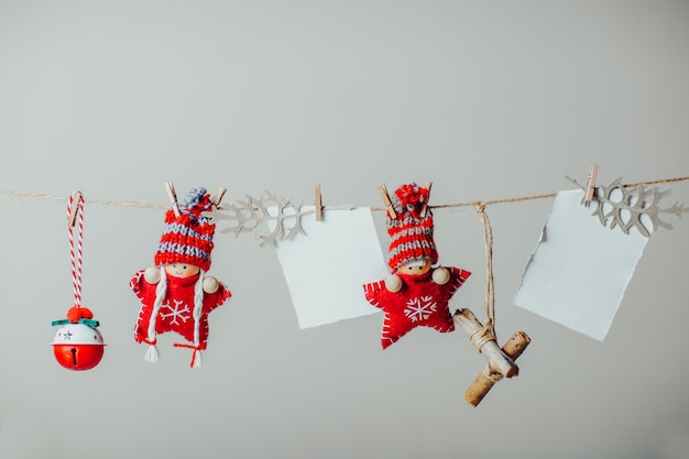 Photo Étoiles de noël tricotées rouges dans des chapeaux drôles. poupées et ornements de noël suspendus à la corde avec une pince à linge. feuille de papier blanc pour le texte.